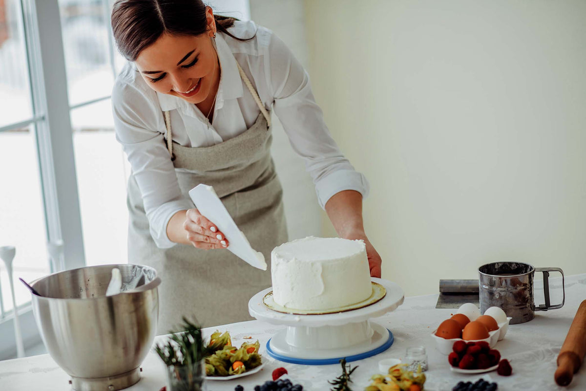 Frau streicht in einer hellen Küche weiße Creme auf eine Torte